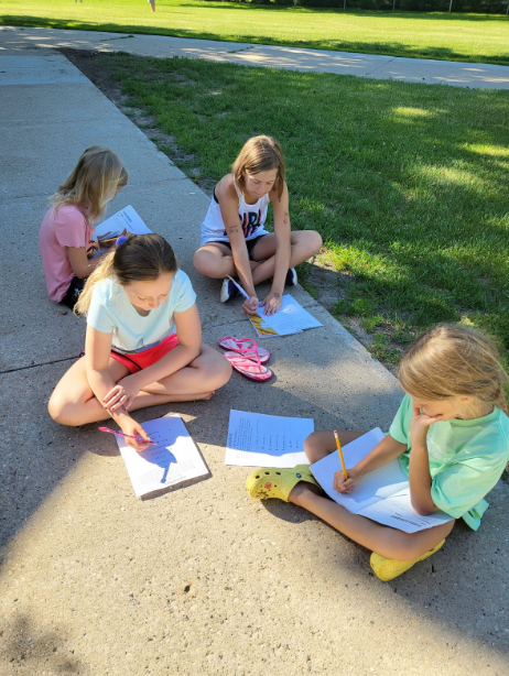Four girls sitting on sidewalk working on papers