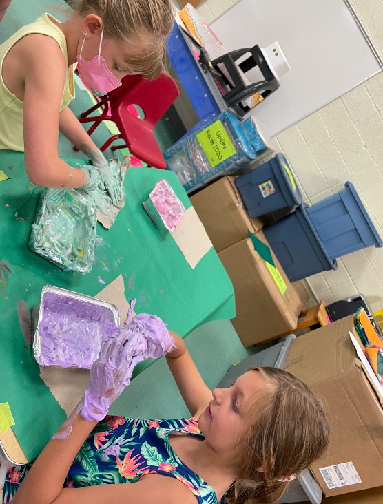 2 girls working at a table with colored shaving cream