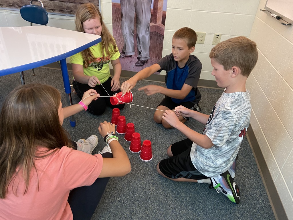 Students building tower of cups using string and rubber band